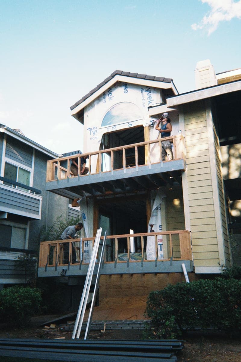 Second-storey balcony framing on a multi-unit building, house wrap exposed and new railings going up.