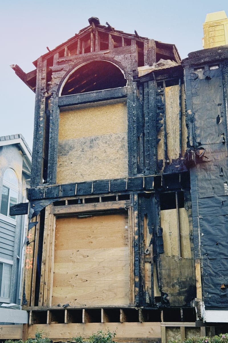 The shell of a burnt-out house, its framing charred black and its window openings boarded over.