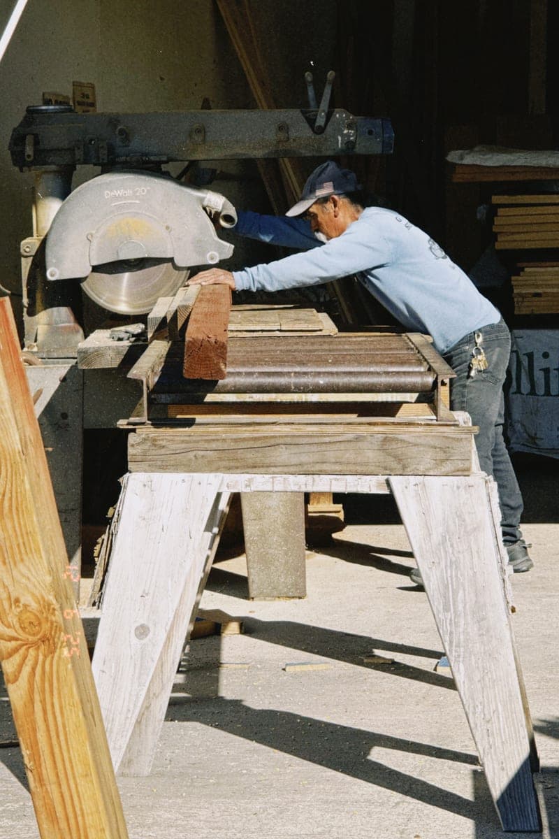 A worker leaning over a mitre saw set up on sawhorses, lining up a length of moulding.
